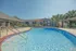 Inviting outdoor pool area with crystal-clear water, surrounded by sun loungers, lush palm trees, and shaded seating, offering a perfect relaxation spot in a beautiful apartment community.
