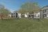 Charming apartment complex with lush green lawn, picnic tables, and beautiful trees under a clear blue sky.