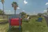 Vibrant outdoor dog park featuring agility equipment, picnic table, and lush green space under a sunny sky with palm trees.