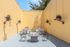 Charming outdoor patio with modern seating, barbecue grills, and cooling fans set against a sunny yellow backdrop.