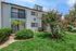 Charming apartment exterior with lush green landscaping and colorful flowering trees, inviting entry, and stylish balcony.