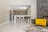 Contemporary open-concept living area featuring a chic bar with modern stools, elegant stone fireplace, and a vibrant yellow lounge chair on glossy marble flooring.