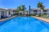 Luxurious apartment complex featuring an inviting swimming pool, sun loungers, and a stylish cabana, surrounded by lush palm trees.