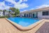 Inviting apartment complex pool area with crystal-clear water, cozy blue chairs, and lush landscaping under a bright blue sky.