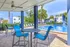 Inviting outdoor seating area with vibrant blue chairs, overlooking a sparkling swimming pool surrounded by lush greenery and residential buildings.