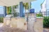 Inviting outdoor barbecue area with modern stainless steel grills on sleek stone countertops, surrounded by lush greenery and palm trees.