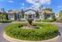 Charming apartment complex entrance with a beautifully landscaped circular hedge and elegant fountain, under a clear blue sky.