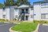 Charming apartment exterior with a welcoming two-story entrance, surrounded by lush greenery and ample parking space.