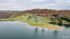Scenic aerial view of a luxury lakeside retreat with a spacious lodge, pristine pool, tennis courts, and lush greenery, nestled amidst serene woodlands.