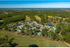 Aerial view of a spacious apartment complex nestled in lush greenery with a clear blue sky backdrop, featuring multiple buildings, a pool area, and serene natural surroundings.