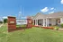 Welcoming exterior of The Heights on Oak with manicured lawns, vibrant red flowers, and a charming brick sign under a bright blue sky. Ideal residential community atmosphere.