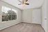 Bright room with plush carpet and ceiling fan, featuring large window offering a charming garden view.