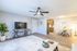 Bright and modern living room with an open layout, featuring a sleek ceiling fan, stylish TV stand, cozy seating area, and an inviting dining space adjacent to the kitchen.