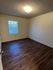 Inviting bedroom with warm wood floors, soft lighting, and a bright window for natural light.