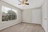 Bright, spacious room with plush carpeting and large window offering a scenic view, complemented by a modern ceiling fan.
