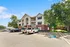 Charming three-story apartment building with classic red brick and modern beige siding, surrounded by lush greenery and ample parking space.