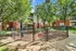 Inviting apartment complex featuring a sunny dog park with benches, surrounded by lush trees and modern brick buildings.