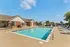 Inviting outdoor pool with comfortable lounge chairs and shade umbrellas, adjacent to a charming brick clubhouse under a clear blue sky.