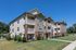 Charming three-story apartment complex featuring elegant balconies, lush green lawn, and modern architectural design under a clear blue sky.