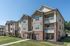 Charming three-story apartment complex with modern balconies, surrounded by lush greenery under a clear blue sky.