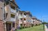 Modern apartment complex with charming brick accents, spacious balconies, and well-maintained green lawns under a clear blue sky.