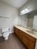 Elegant bathroom with spacious vanity, warm wooden cabinetry, large mirror, and modern lighting.