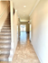 Bright, inviting hallway with elegant tile flooring leading to a sunlit room, featuring a carpeted staircase and modern lighting.