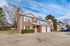 Charming red brick townhouse with large windows and spacious driveway, nestled in a serene neighborhood surrounded by lush trees.