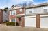 Charming two-story brick townhouse with a double garage, surrounded by greenery and featuring large windows for natural light.