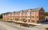 Charming red-brick apartment complex with modern design and ample parking, bathed in sunlight against a clear blue sky.