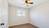 Bright bedroom with elegant ceiling fan, natural light from a charming window, and sleek wooden flooring.