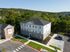 Charming multi-story apartment complex surrounded by lush greenery, featuring modern design and ample parking spaces.