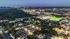 Stunning aerial view of a vibrant urban neighborhood illuminated at dusk, showcasing a blend of residential areas, green spaces, and a well-lit sports field.