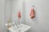 Bright and modern bathroom with elegant fixtures, featuring a sleek white sink, warm lighting, and a stylish coral hand towel.