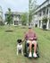 Inviting apartment complex with lush green surroundings, featuring a person in a wheelchair smiling with their dog, highlighting accessible pathways and vibrant community living.