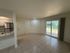 Bright and airy living room with modern tile flooring, sliding glass doors, and a view of lush greenery, adjacent to a sleek kitchen area.