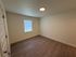 Bright bedroom with modern wood flooring, creamy walls, and ample natural light from a large window.