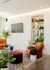 Modern living room with white brick wall, sleek TV, leather seating, glass coffee table, and lush green plants.