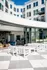 Modern apartment building with large glass windows and a stylish outdoor seating area, offering an inviting space for relaxation and social gatherings.