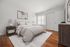 Inviting bedroom with cozy bed, elegant nightstands, and natural light from a large window, complemented by warm wooden floors.