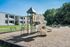 Inviting playground with slides and climbing structures, set against a backdrop of modern apartments and lush greenery.