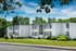 Charming two-story apartment building surrounded by lush greenery and manicured lawns under a bright blue sky.