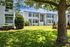 Charming apartment complex with bright white exterior, lush green lawn, and beautiful landscaping under a sunny blue sky.