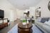 Elegant living room with cozy gray sofa, vibrant cushions, stylish coffee table, and open-concept kitchen with chic bar seating.