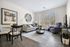 Bright and modern living room with elegant decor, featuring a cozy gray sofa, sleek round mirror, and stylish artwork. Large windows offer plenty of natural light, illuminating the chic furnishings and inviting atmosphere.