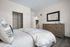 Inviting bedroom with sleek hardwood floors, modern dresser, plush bed, and a glimpse of a cozy kitchen.