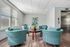Inviting lounge area with elegant teal armchairs, a round wooden table, and abundant natural light from large windows, perfect for relaxation and conversation.