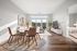 Bright and inviting open-plan living and dining area with elegant decor, hardwood floors, and large windows offering scenic views, next to a cozy bedroom.