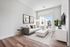 Bright, modern living room featuring elegant wooden flooring, a plush sofa with decorative cushions, a sleek white coffee table, and natural light streaming through large glass doors.