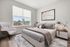 Bright and inviting bedroom with modern decor, featuring a plush bed, chic side table, and a cozy stylish armchair, complemented by a large window offering scenic views.